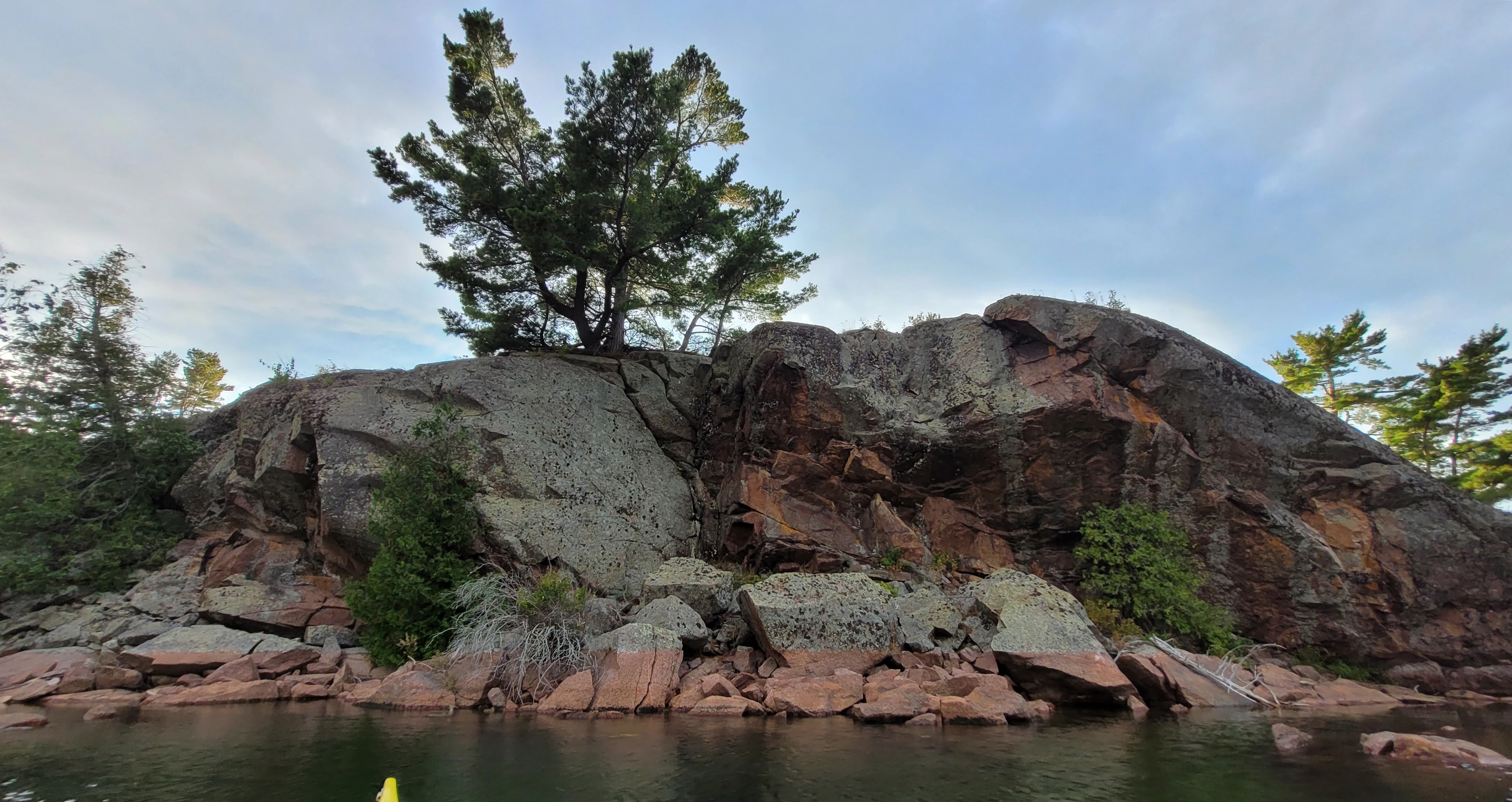 A calm cove red cliff with a tree on top in North Benjamin Island in The North Channel of Lake Huron
